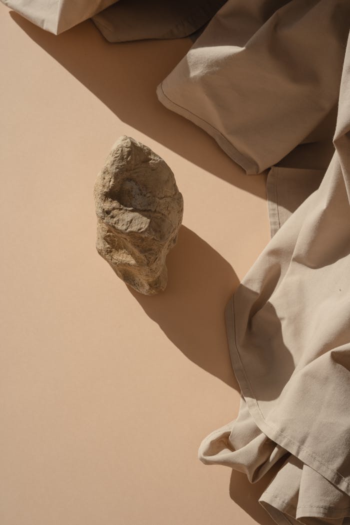 A beige stone cast in shadow on a draped fabric background, minimalist style.